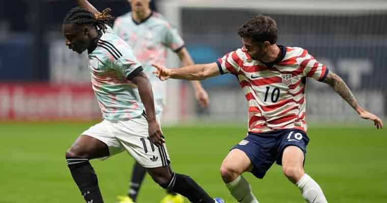 Two soccer players sprint for the ball during a match: one in a mint jersey and black shorts, the other in a red‑and‑white USA kit reaching with his leg. Two players chase the ball on a green field in a tense moment of play, one in mint and black, the other in red‑and‑white stripes (USA).